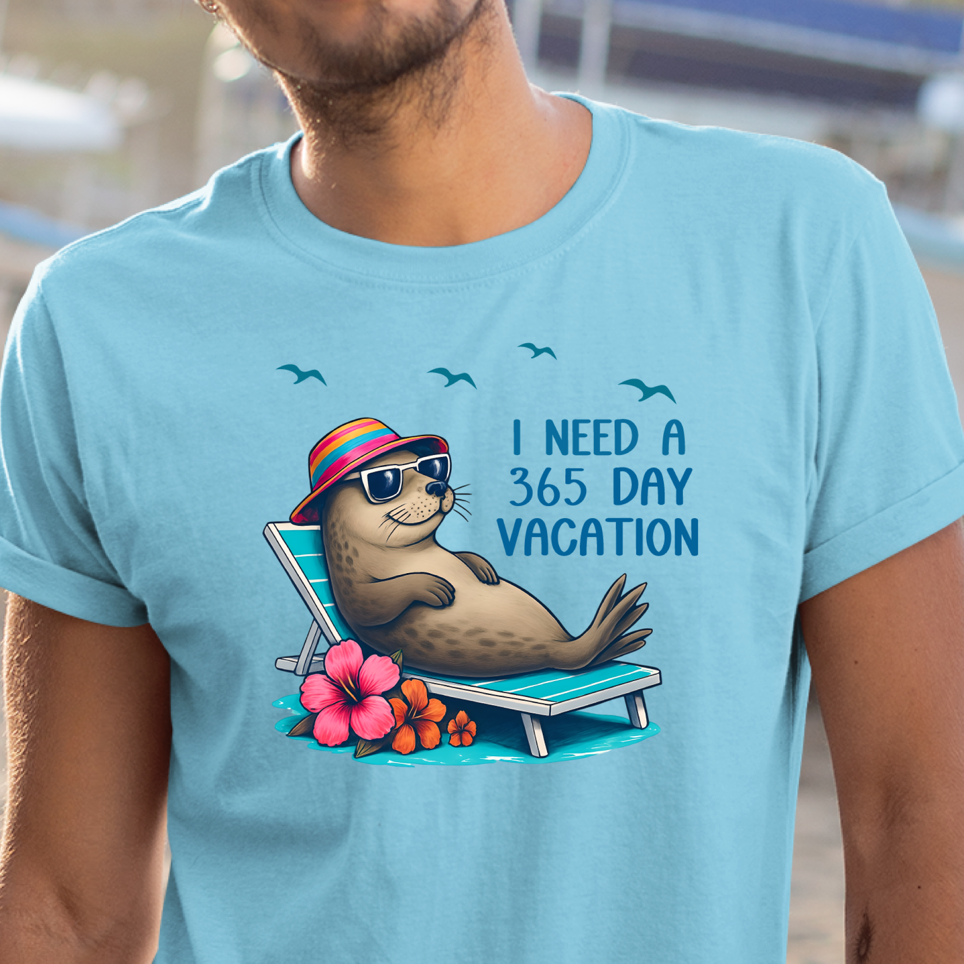 Person wearing a sky blue t-shirt with a seal graphic and text 'I Need a 365 Day Vacation'.