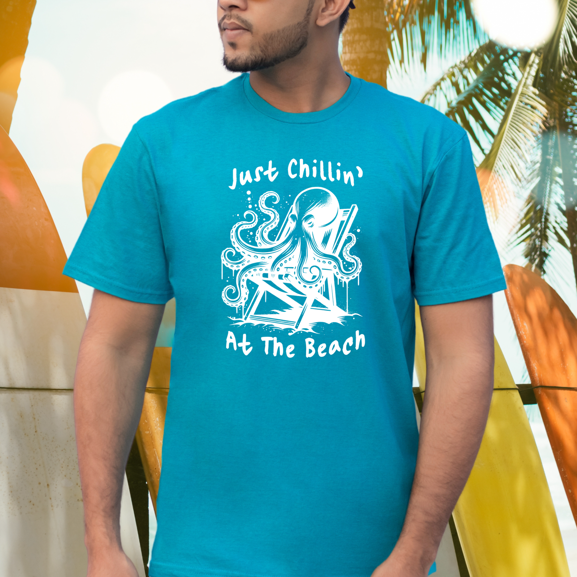 Gildan 5000 "Just Chillin' At The Beach" t shirt with an octopus setting in a beach chair in one color graphics. Picture of a man standing by surfboards wearing a t shirt.