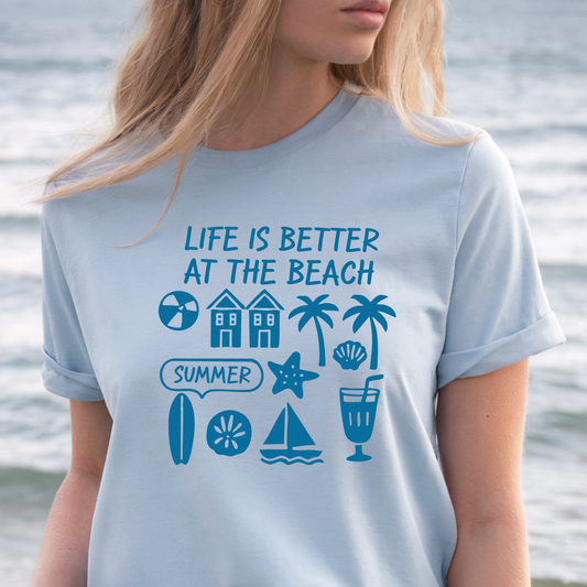 Person wearing a light blue t-shirt with beach-themed graphics and text by the water.