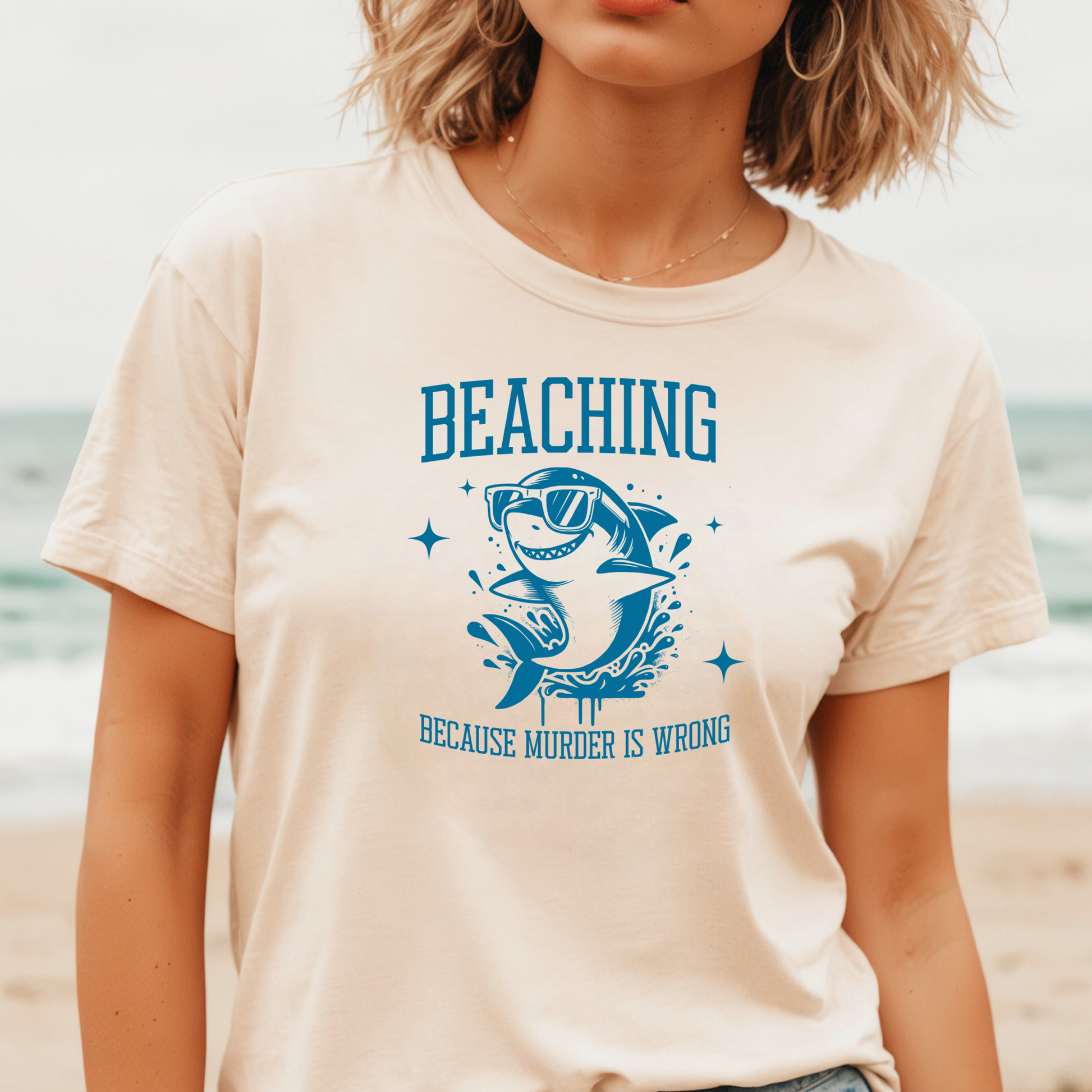 Gildan 5000 "Beaching Because Murder Is Wrong" t shirt with a funny shark with sunglasses jumping out of water in one color graphics. Picture of a girl standing on the beach wearing a t shirt.