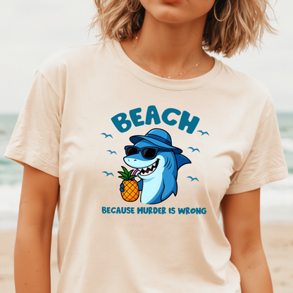 Person wearing a t-shirt with a shark graphic and text on a beach.