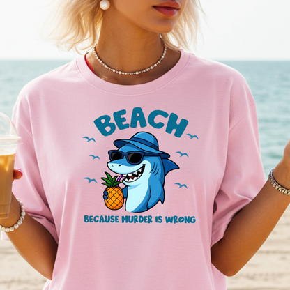 Person wearing a pink t-shirt with a shark graphic and 'BEACH BECAUSE MURDER IS WRONG' text on a beach.
