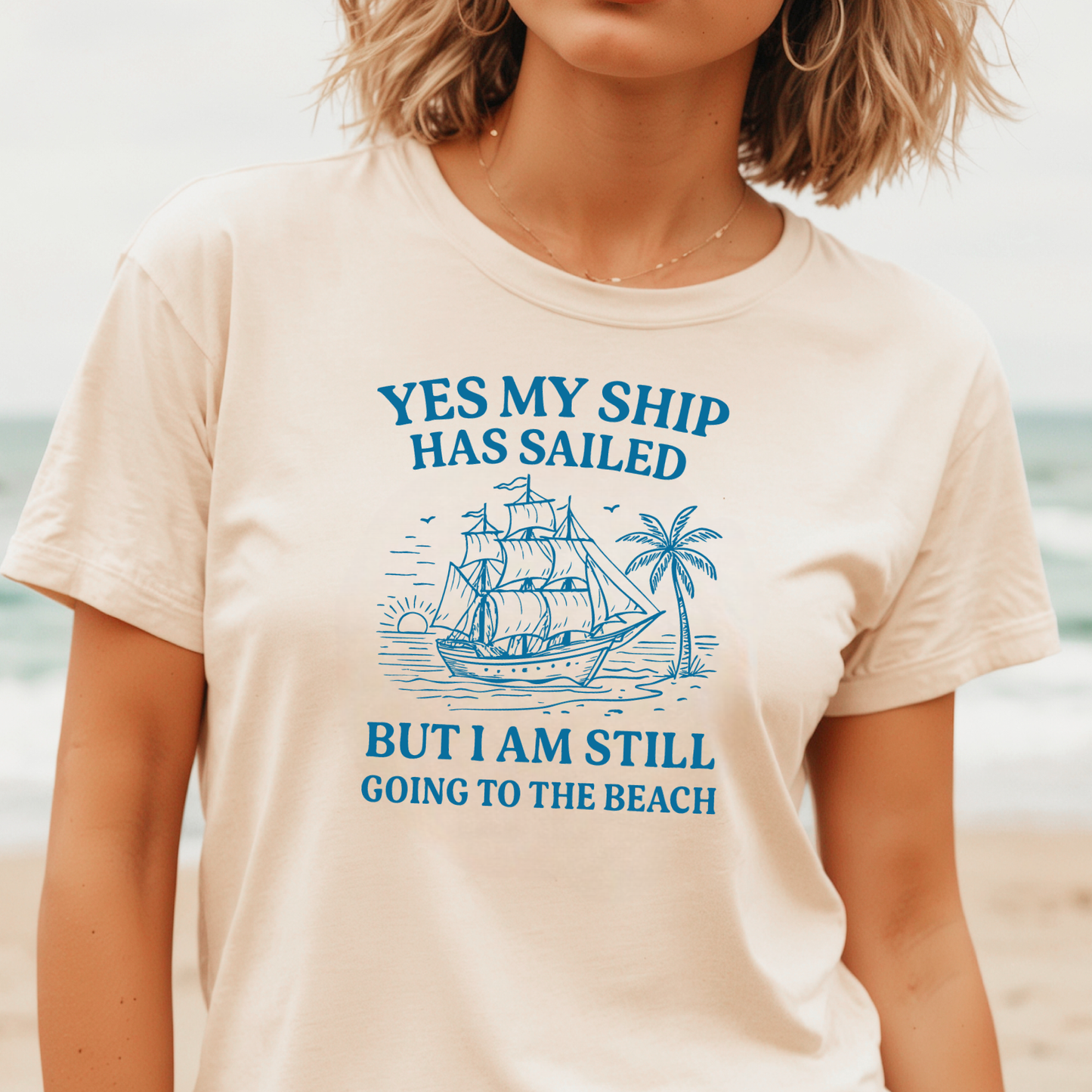 Person wearing a t-shirt with a ship and beach graphic and text on a beach background