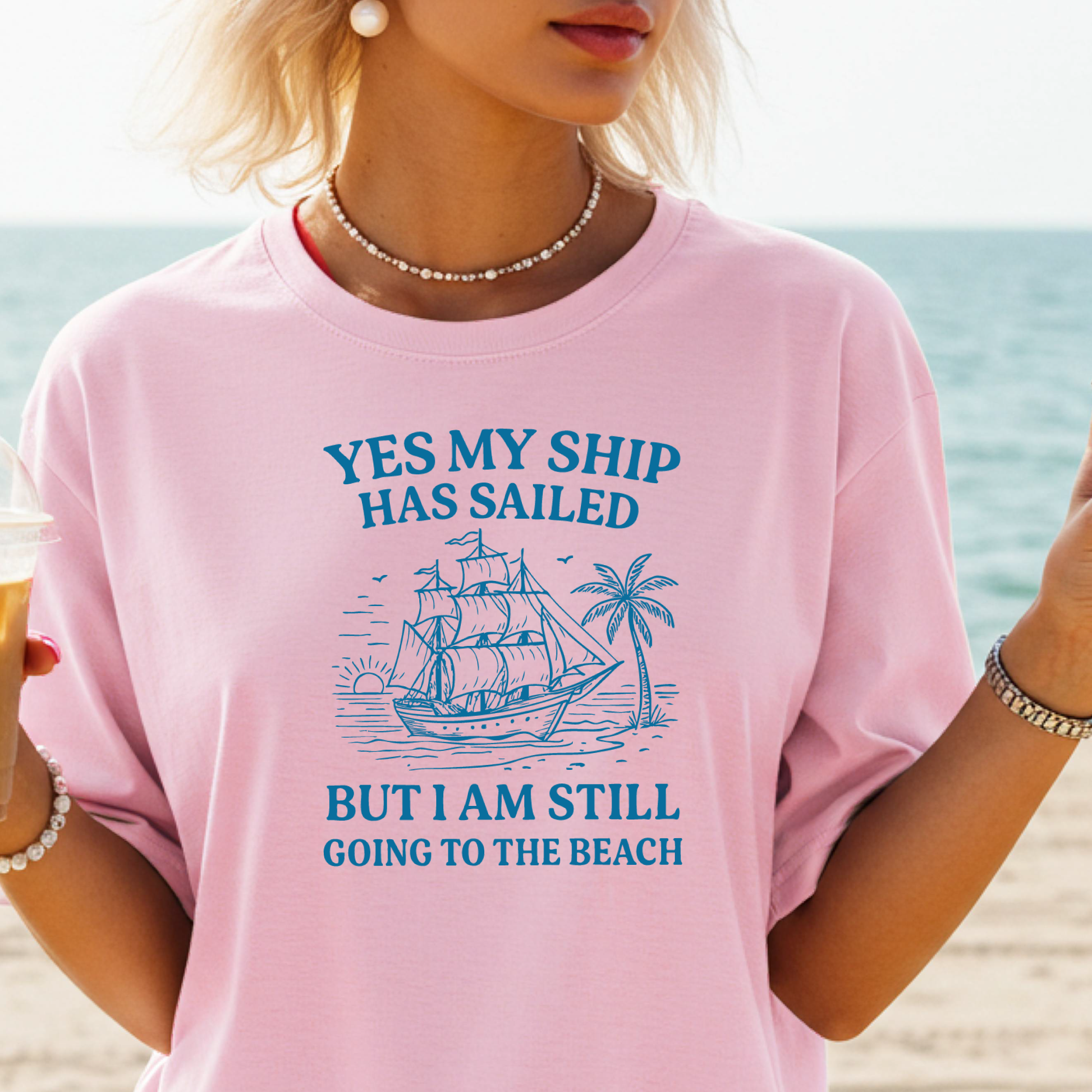 Person wearing a pink t-shirt with a beach-themed design and text on a beach background