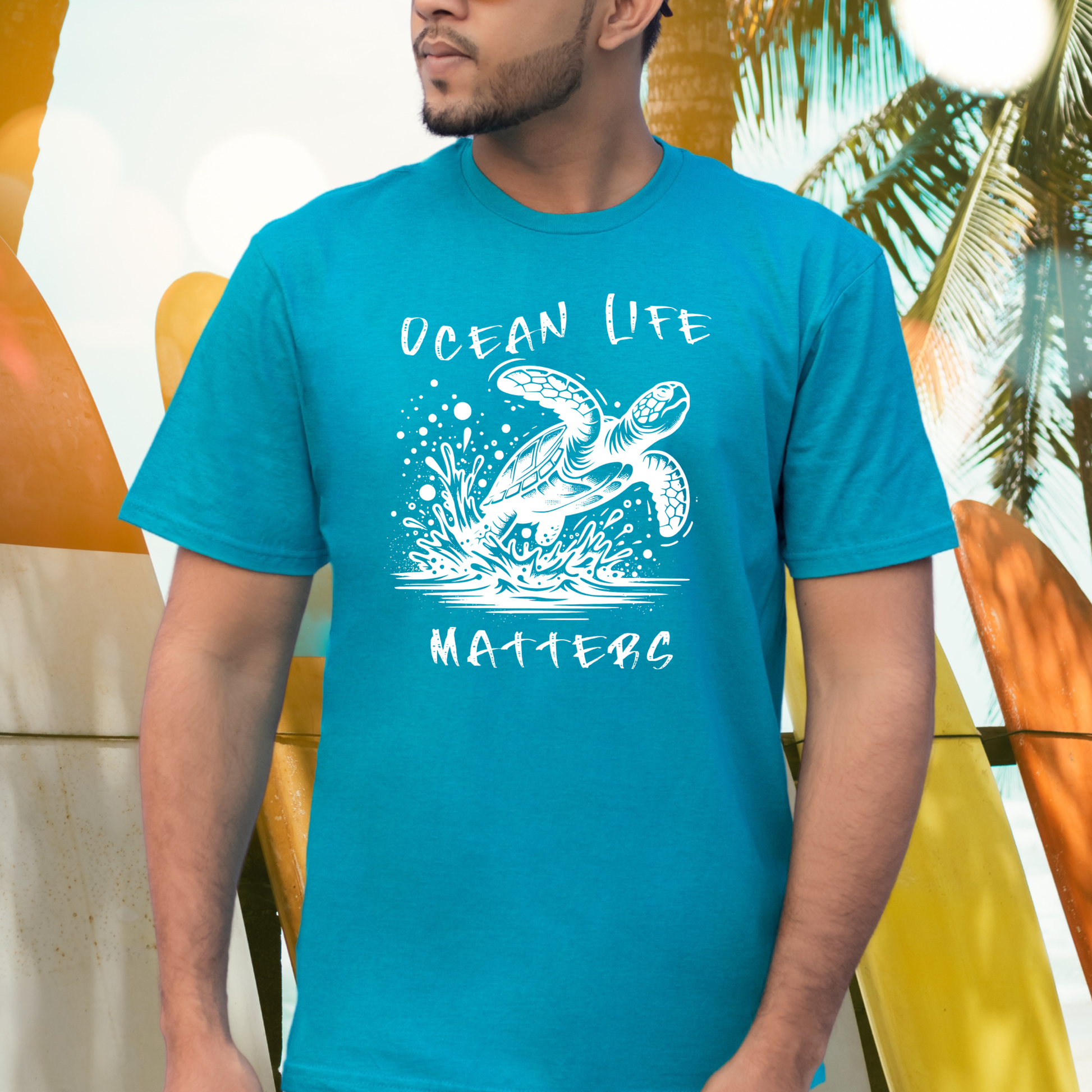 Gildan 5000 "Save The Ocean and The Sea Life In It" t shirt with a sea turtle splashing in water in a one color graphic. Picture of a man standing next to surfboards wearing a t shirt.