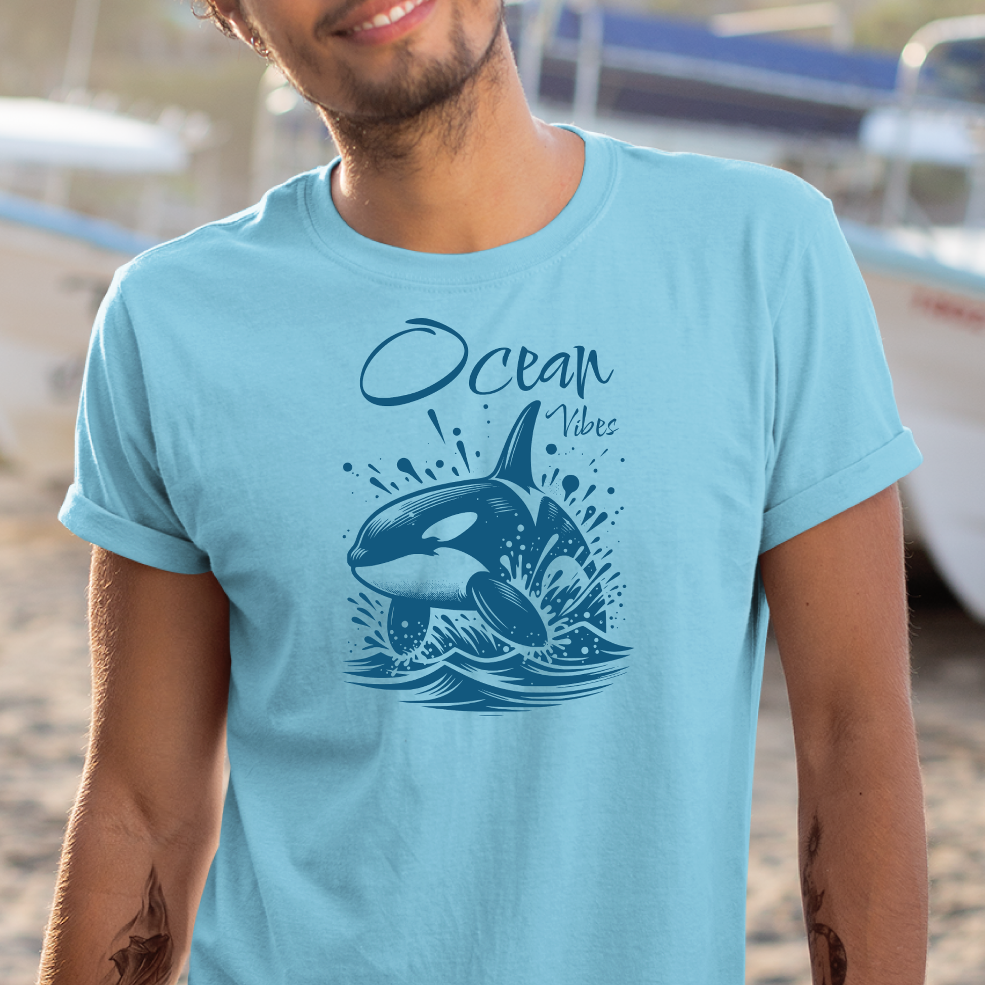 Gildan 5000 "Ocean Vibes" t shirt with a orca whale jumping out of water graphics in a one color graphic. Picture of a man standing in a boat yard wearing a t shirt.