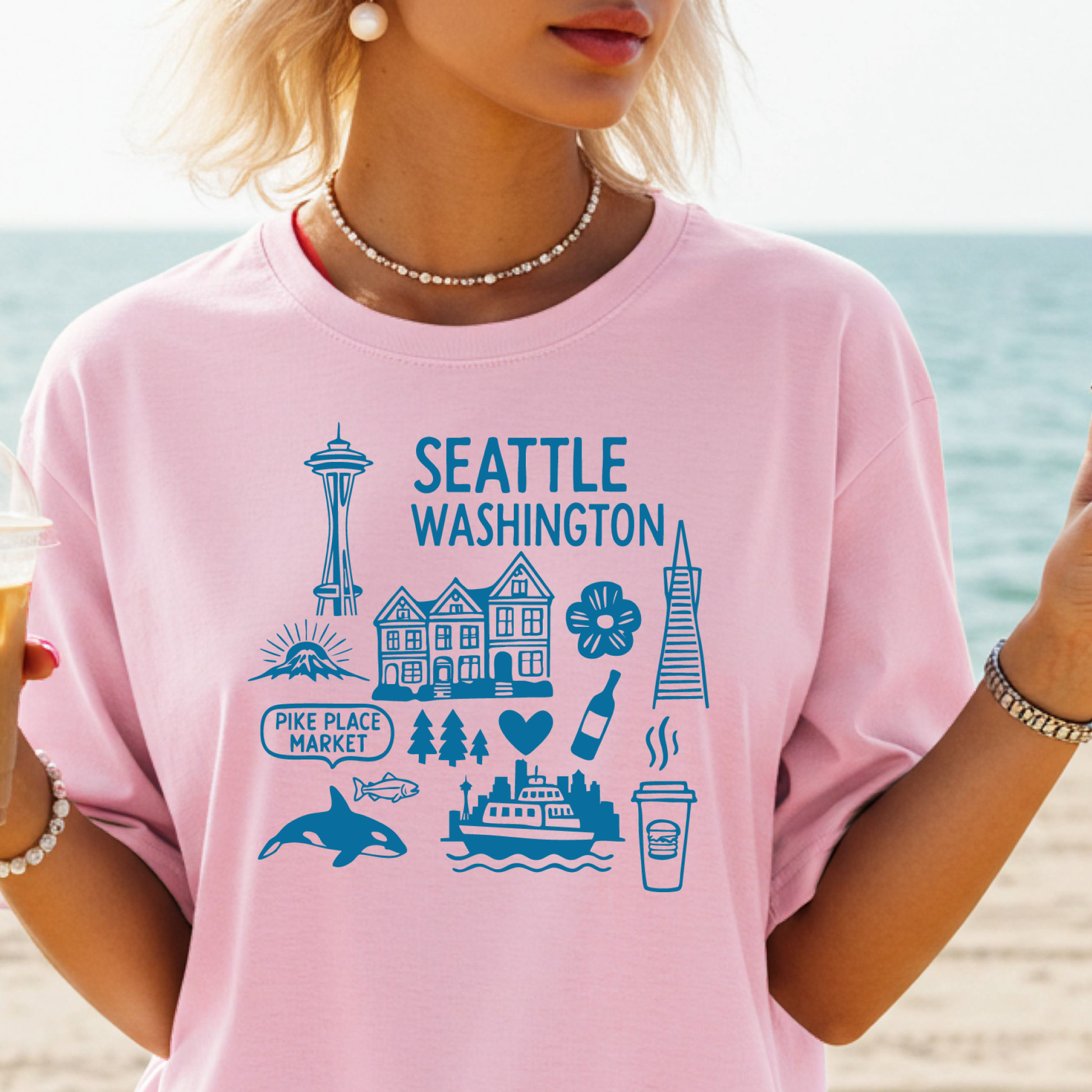 Person wearing a pink t-shirt with Seattle-themed graphics on a beach.