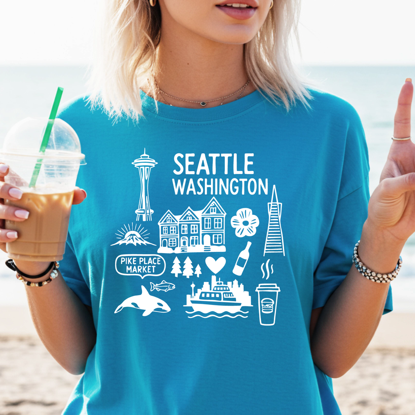 Person wearing a blue t-shirt with Seattle-themed graphics on a beach.