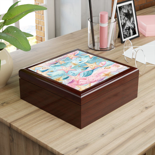The Starfish Beach Jewelry Box - Coastal Charm for Ocean Lovers, with its colorful sea-themed starfish design on a glossy lid, sits on a wooden desk beside reading glasses, a pen holder with pens, and a plant. A window in the background lets in natural light.