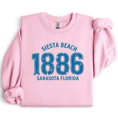 Pink sweatshirt with blue text 'Siesta Beach 1886 Sarasota Florida' on a white background