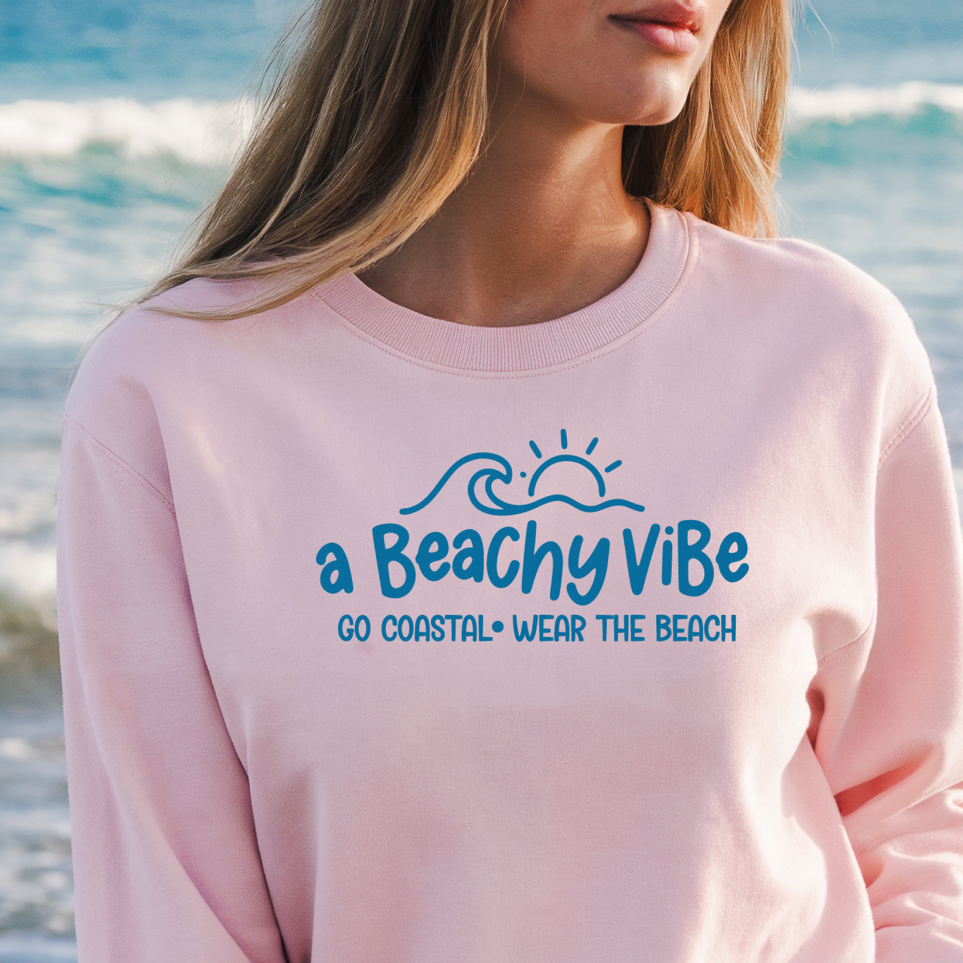 Person wearing a pink sweatshirt with 'a Beachy Vibe' text at the beach