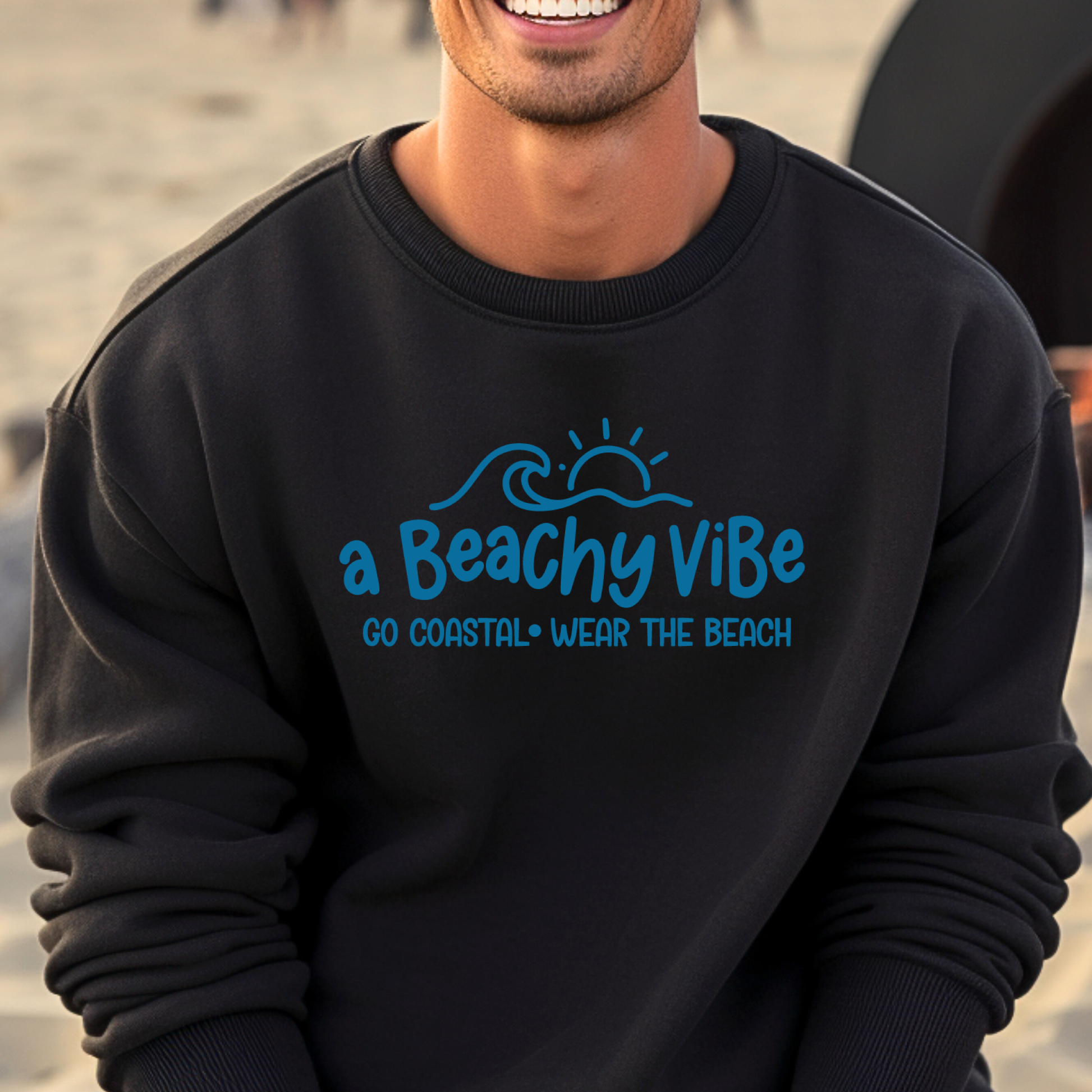 Person wearing a black sweatshirt with blue text and graphics on a beach.