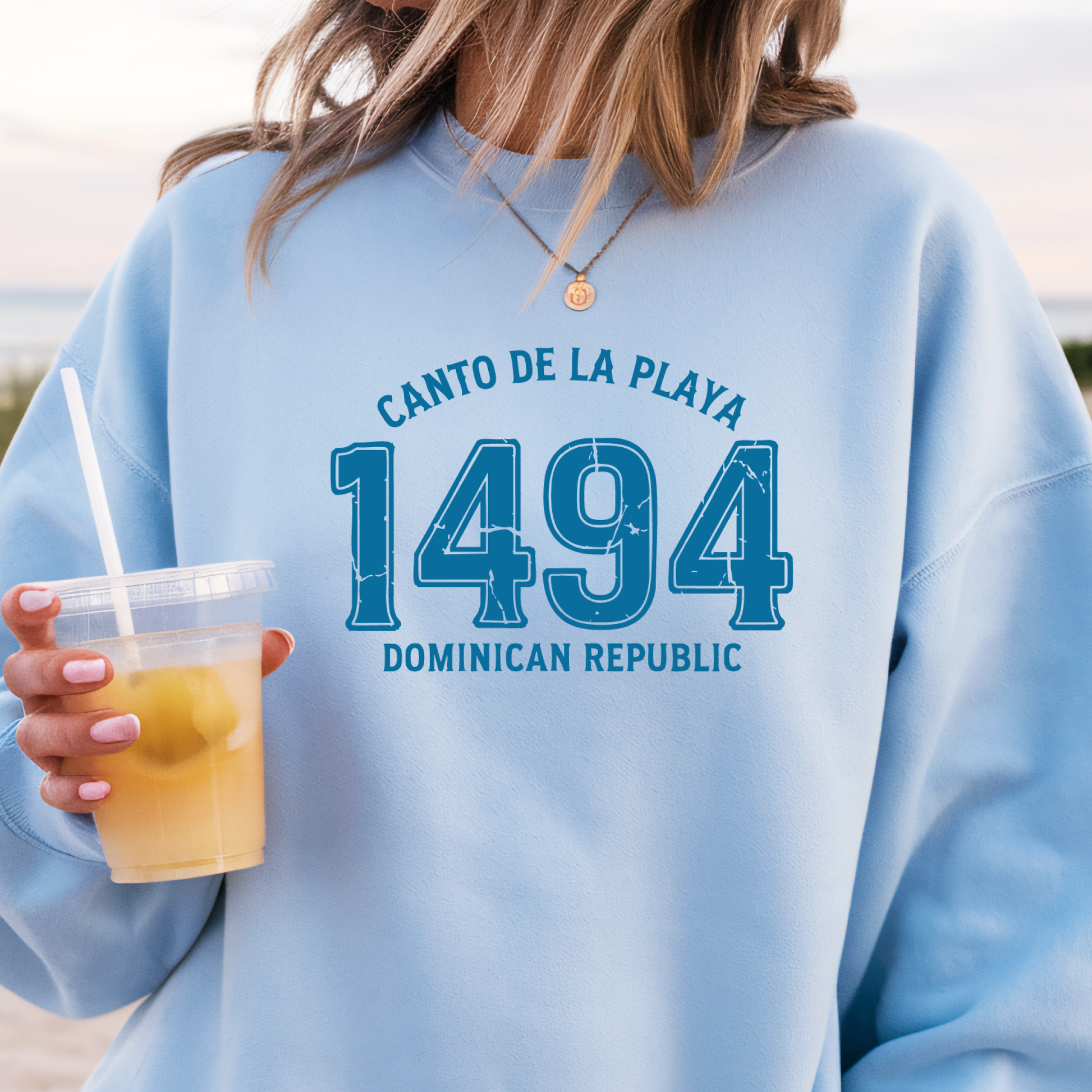 Gildan sweatshirt with “Canto De La Playa 1494 Dominican Republic” printed in distressed navy text. Vintage beach-inspired crewneck symbolizing Caribbean heritage and coastal charm. Made from soft cotton-poly blend fabric for comfort and style, ideal for beach lovers and travelers who adore Dominican culture. Cozy, sustainable, and perfect for casual wear or tropical getaways.
