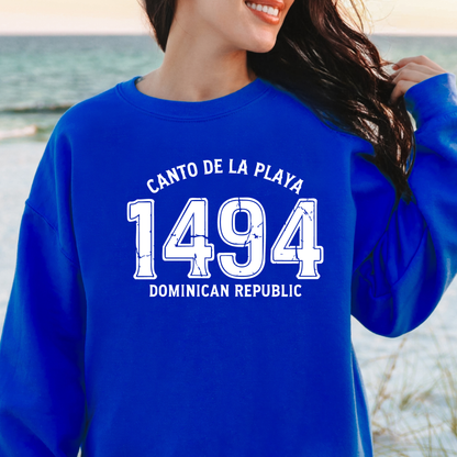 Gildan sweatshirt with “Canto De La Playa 1494 Dominican Republic” printed in distressed navy text. Vintage beach-inspired crewneck symbolizing Caribbean heritage and coastal charm. Made from soft cotton-poly blend fabric for comfort and style, ideal for beach lovers and travelers who adore Dominican culture. Cozy, sustainable, and perfect for casual wear or tropical getaways.