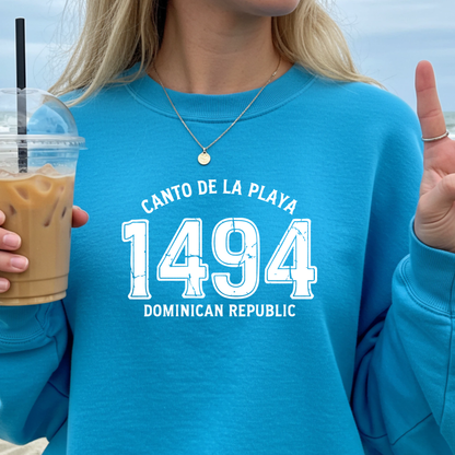 Gildan sweatshirt with “Canto De La Playa 1494 Dominican Republic” printed in distressed navy text. Vintage beach-inspired crewneck symbolizing Caribbean heritage and coastal charm. Made from soft cotton-poly blend fabric for comfort and style, ideal for beach lovers and travelers who adore Dominican culture. Cozy, sustainable, and perfect for casual wear or tropical getaways.