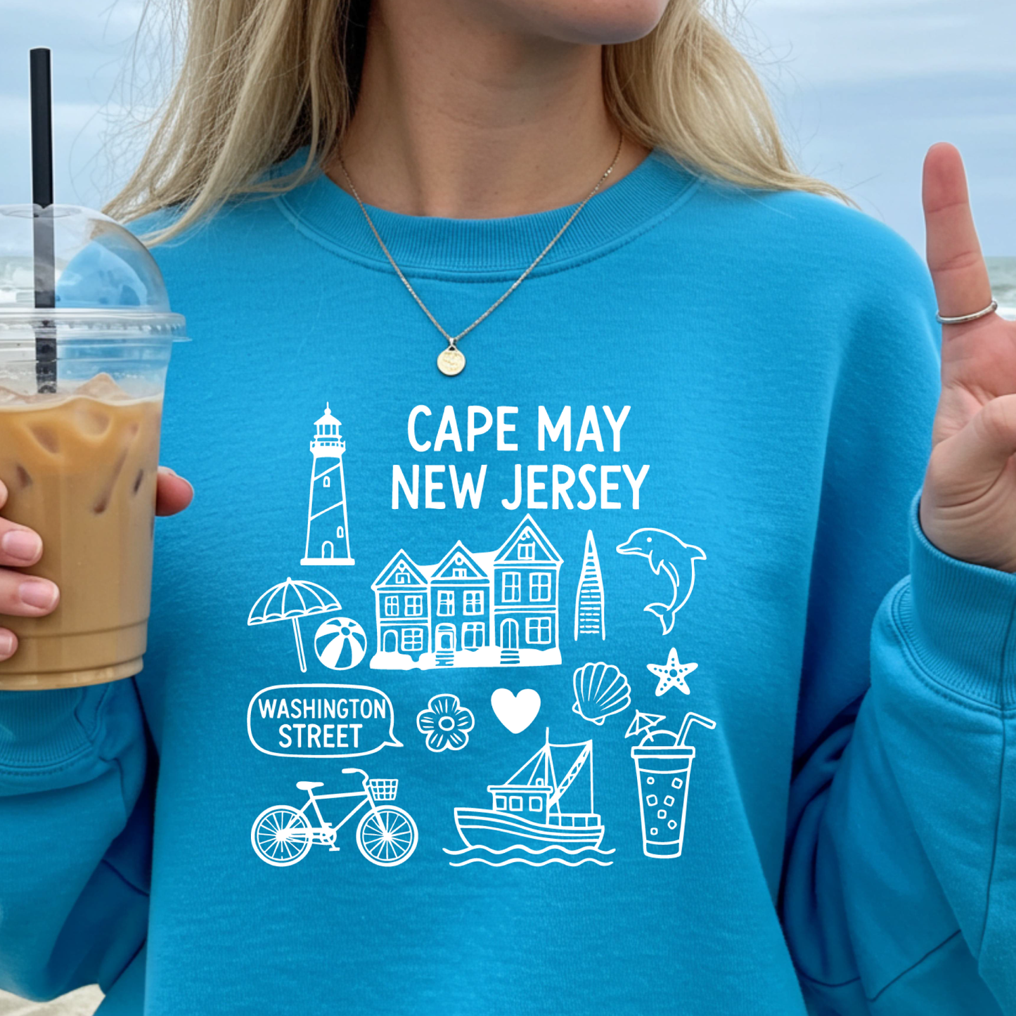 Gildan sweatshirt with blue Cape May New Jersey design featuring beach icons like a lighthouse, dolphin, beach ball, shells, and Washington Street sign. Coastal-inspired pullover made from soft cotton-poly blend fabric, ideal for beach lovers and Cape May fans. Perfect for seaside getaways or relaxing at home, this cozy crewneck celebrates the charm of New Jersey’s iconic coastal town.