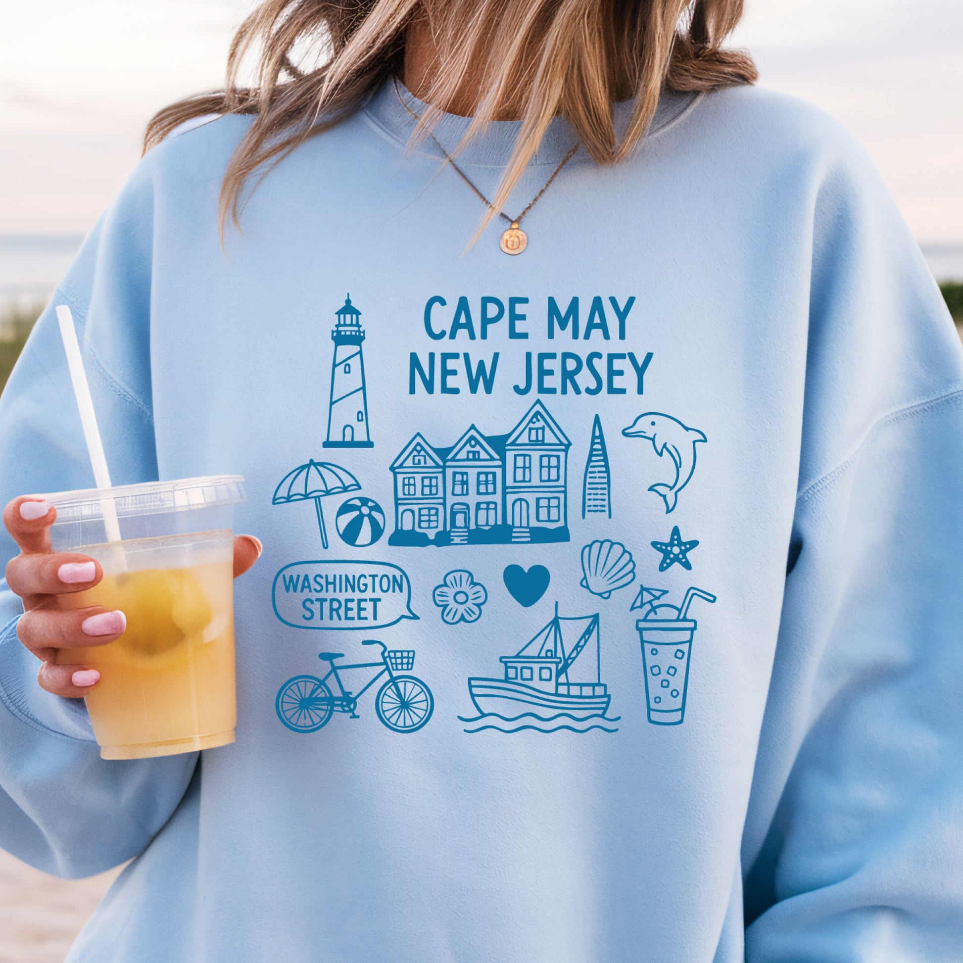Gildan sweatshirt with blue Cape May New Jersey design featuring beach icons like a lighthouse, dolphin, beach ball, shells, and Washington Street sign. Coastal-inspired pullover made from soft cotton-poly blend fabric, ideal for beach lovers and Cape May fans. Perfect for seaside getaways or relaxing at home, this cozy crewneck celebrates the charm of New Jersey’s iconic coastal town.