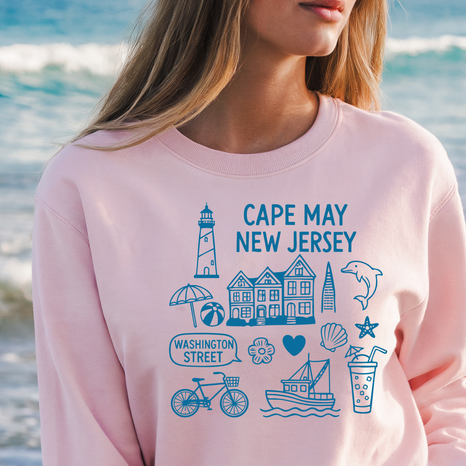Gildan sweatshirt with blue Cape May New Jersey design featuring beach icons like a lighthouse, dolphin, beach ball, shells, and Washington Street sign. Coastal-inspired pullover made from soft cotton-poly blend fabric, ideal for beach lovers and Cape May fans. Perfect for seaside getaways or relaxing at home, this cozy crewneck celebrates the charm of New Jersey’s iconic coastal town.