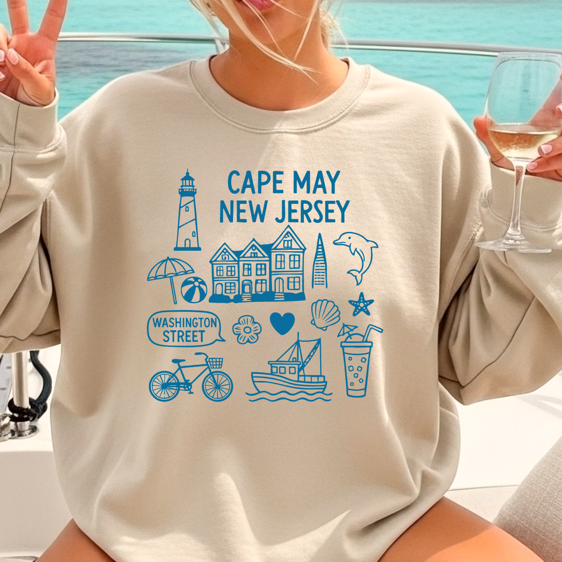 Gildan sweatshirt with blue Cape May New Jersey design featuring beach icons like a lighthouse, dolphin, beach ball, shells, and Washington Street sign. Coastal-inspired pullover made from soft cotton-poly blend fabric, ideal for beach lovers and Cape May fans. Perfect for seaside getaways or relaxing at home, this cozy crewneck celebrates the charm of New Jersey’s iconic coastal town.