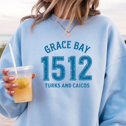 Gildan sweatshirt featuring blue text that reads “Grace Bay 1512 Turks and Caicos” in a vintage collegiate style. Cozy cotton-poly blend pullover with ribbed cuffs and waistband for a relaxed, durable fit. Ideal for beach lovers, island travelers, and fans of coastal fashion. Perfect for staying cozy while showcasing love for one of the Caribbean’s most beautiful beaches — Grace Bay.