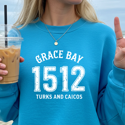 Gildan sweatshirt featuring blue text that reads “Grace Bay 1512 Turks and Caicos” in a vintage collegiate style. Cozy cotton-poly blend pullover with ribbed cuffs and waistband for a relaxed, durable fit. Ideal for beach lovers, island travelers, and fans of coastal fashion. Perfect for staying cozy while showcasing love for one of the Caribbean’s most beautiful beaches — Grace Bay.