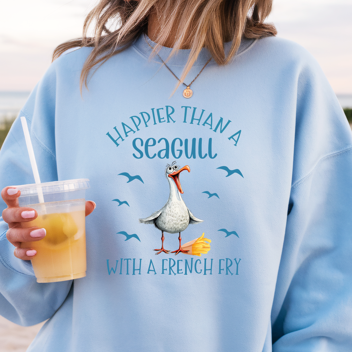 Person wearing a light blue sweatshirt with a seagull graphic and text, holding a drink.