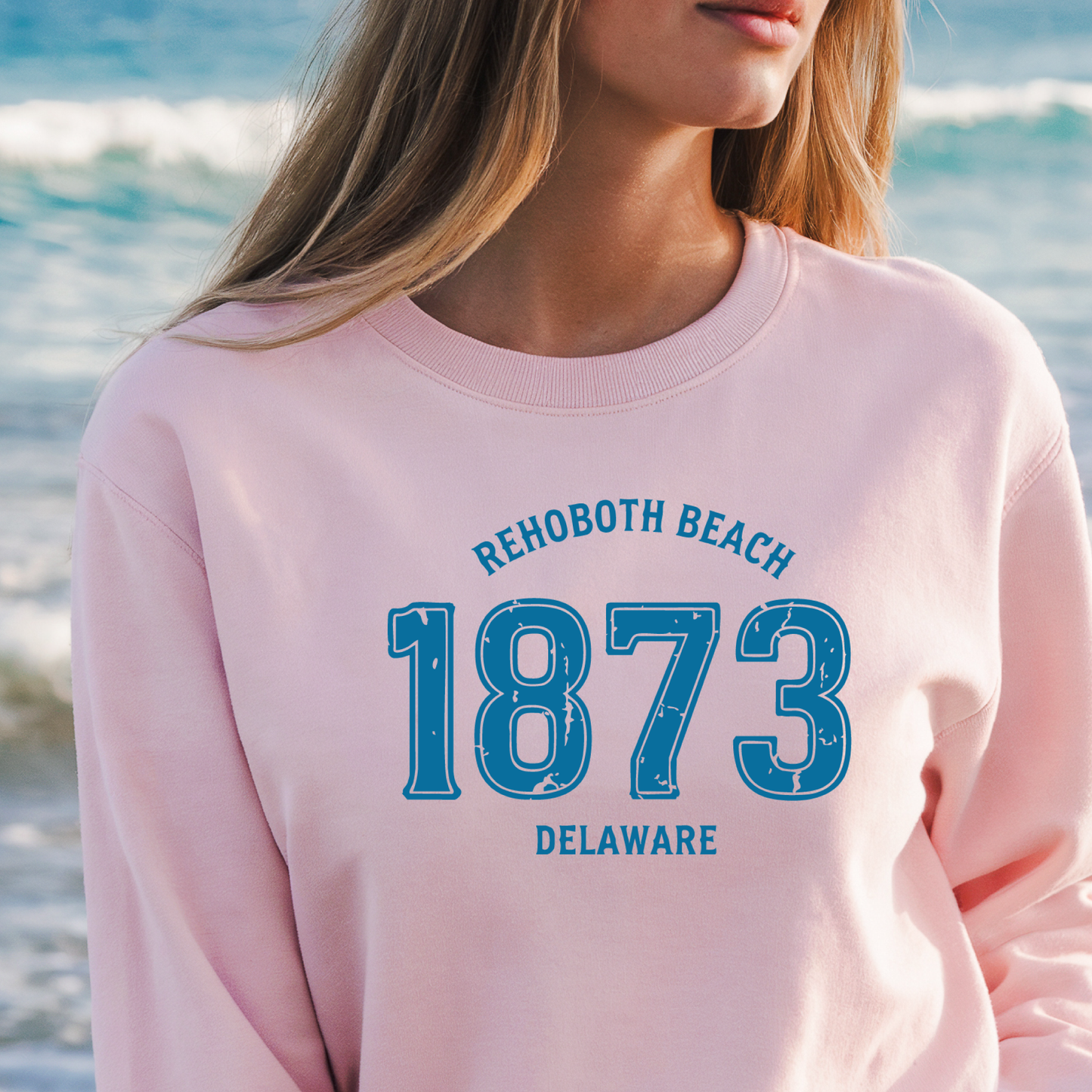 Person wearing a pink sweatshirt with 'Rehoboth Beach 1873 Delaware' text at the beach.