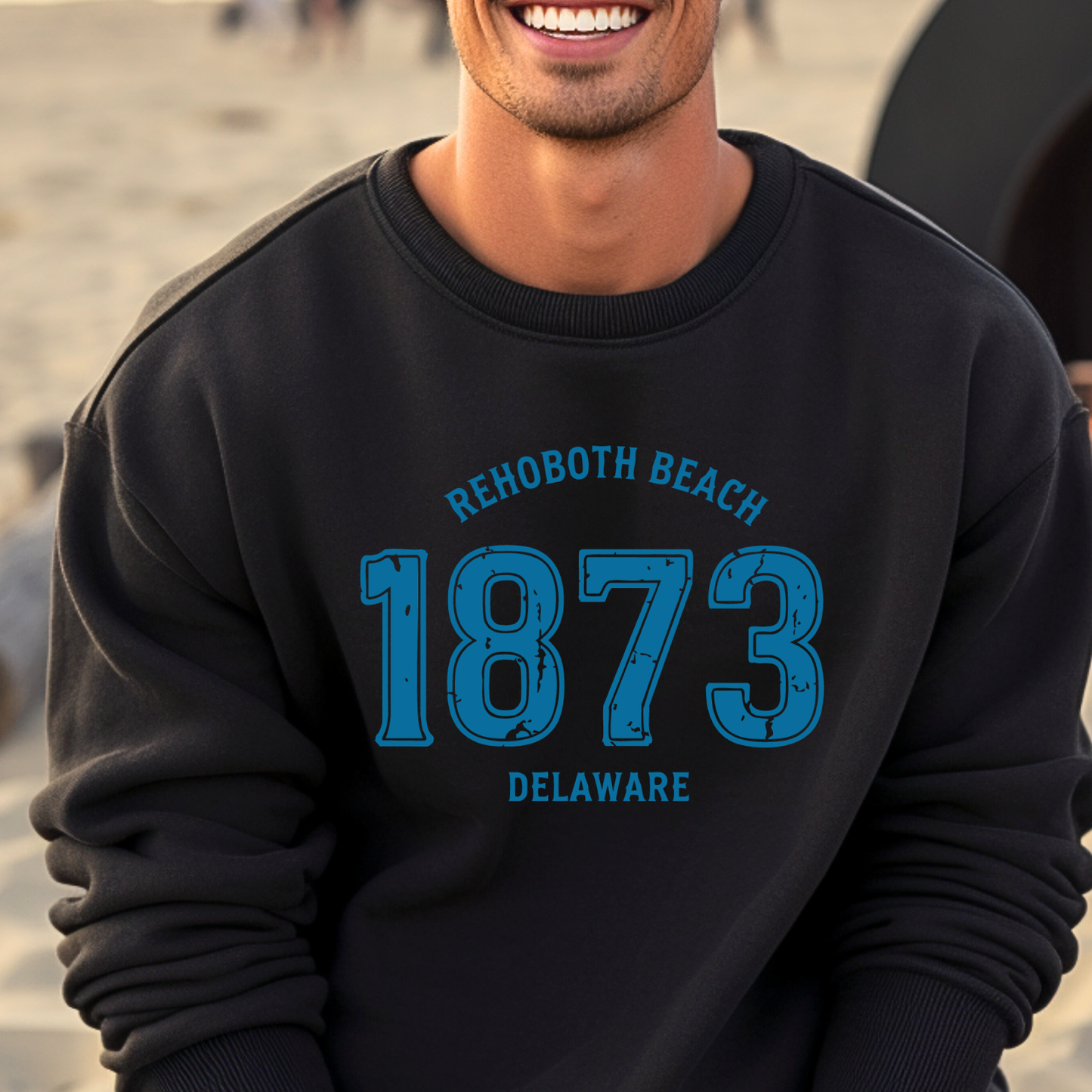 Person wearing a black sweatshirt with 'Rehoboth Beach 1873 Delaware' text on a beach.