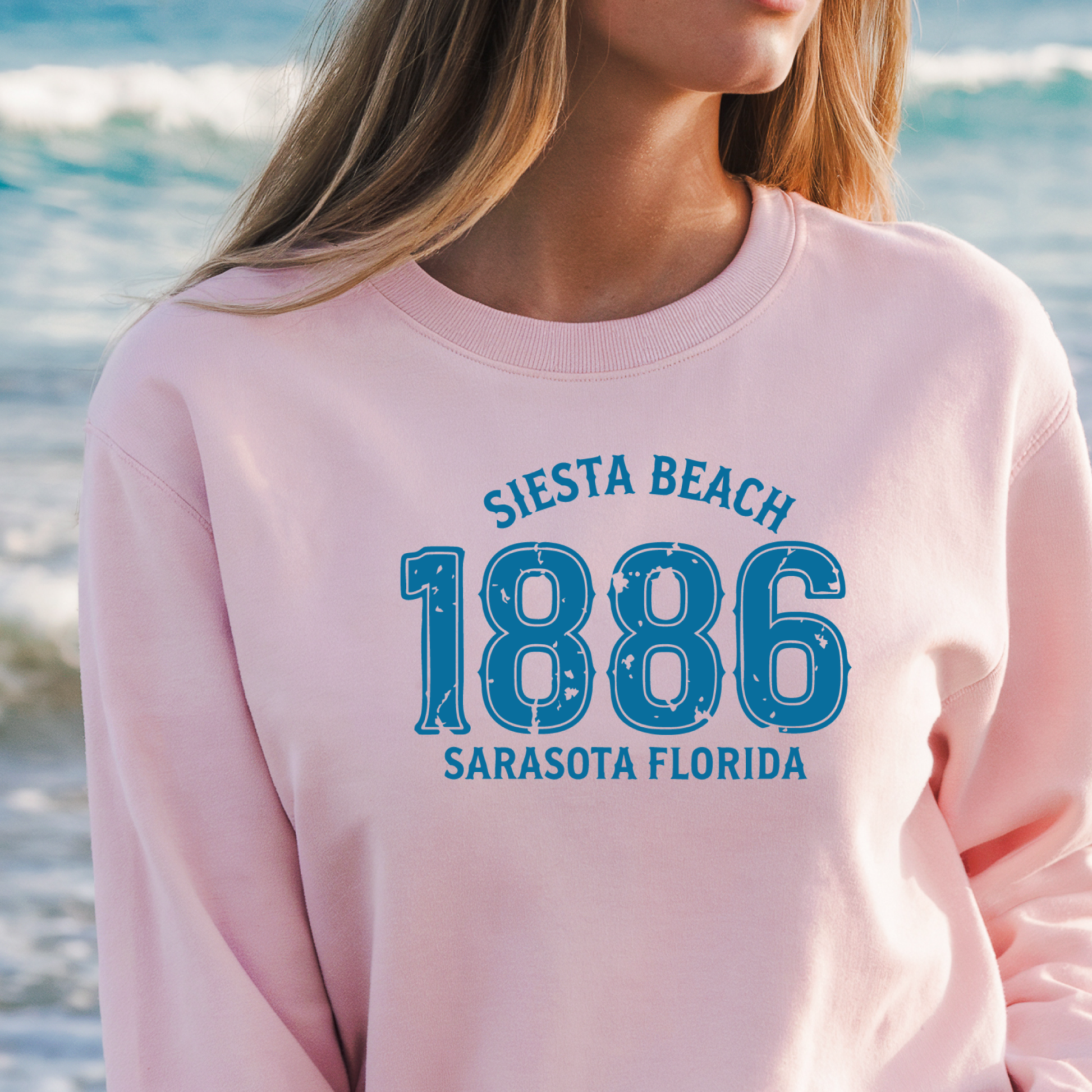 Person wearing a pink sweatshirt with 'Siesta Beach 1886 Sarasota Florida' text on a beach background