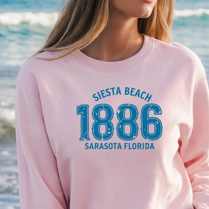 Person wearing a pink sweatshirt with 'Siesta Beach 1886 Sarasota Florida' text on a beach background